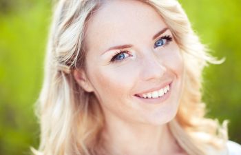 A blond woman with blue eyes is smiling.