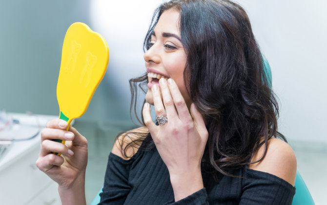 Satisfied woman in a dental chair looking at her teeth after dental treatment in a mirror.