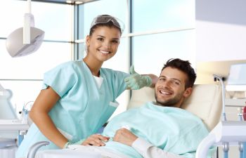 A female dentist and a smiling man sitting in a dental chair.