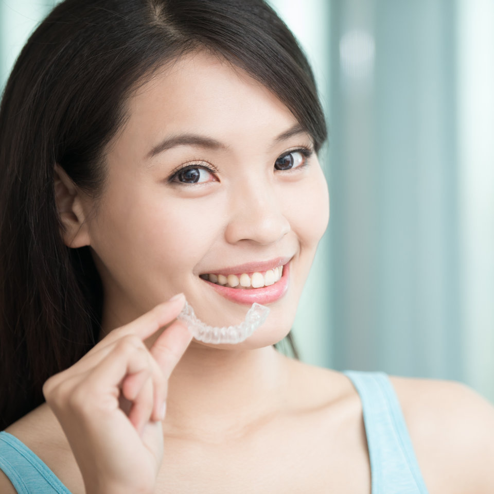 A woman is smiling while wearing a clear aligner.