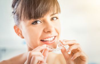 A woman with a perfect smile holding a clear orthodontic aligner