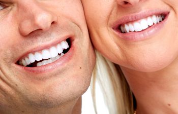 Close-up of two people smiling, showing their white teeth. Only the lower part of their faces is visible.