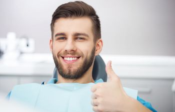 Happy man in a dental chair showing his thumb up