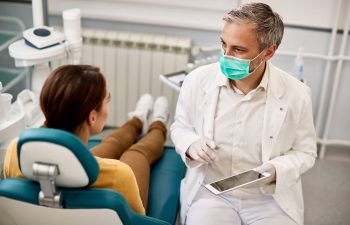 A dentist using a tablet talking to a female patient sitting in a dental chair
